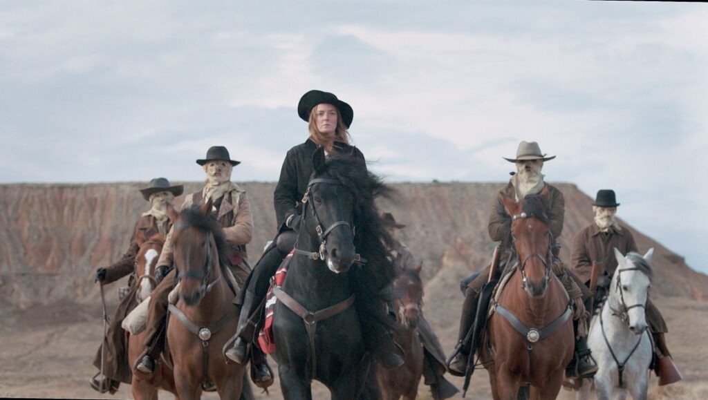 Savage State movie scene. Group of riders on horseback in the Wild West. Woman with black hat on black horse.