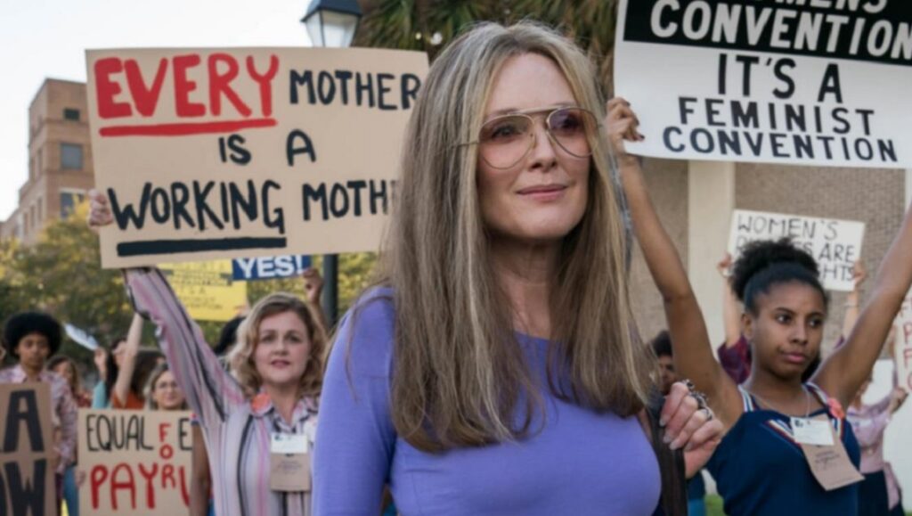 The Glorias | Julie Taymor The Glorias movie scene: Julie Taymor film featuring feminist activists at a convention, holding signs for equal rights.