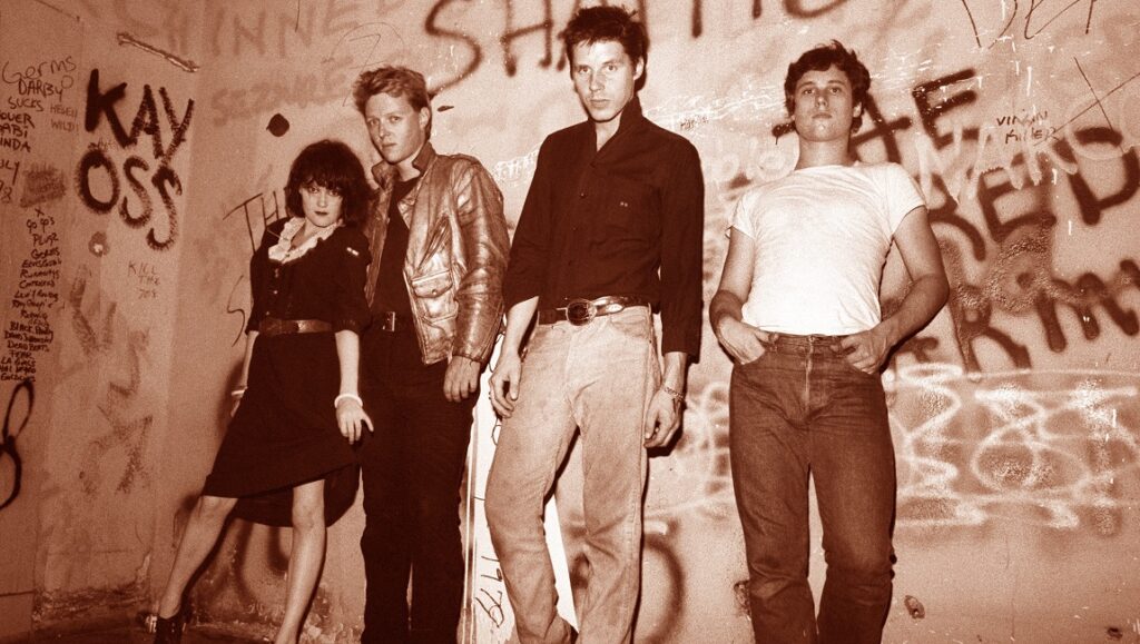 X band, Wild Gift era. Sepia-toned shot of the punk rock band against graffiti wall. 1980s music scene.