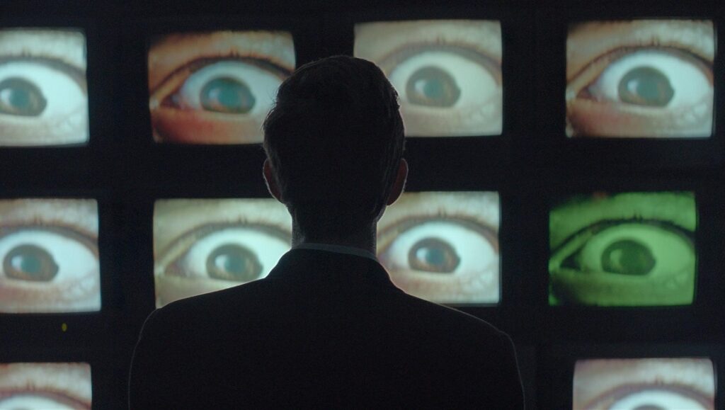 The Antenna film still. Man watches screens displaying eyes. Surveillance concept.