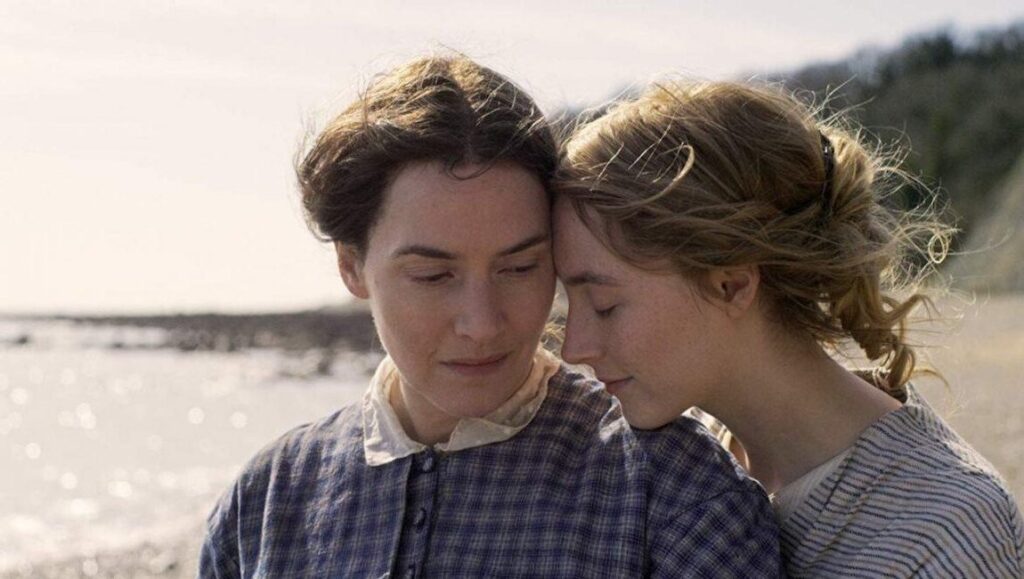 Ammonite film scene: Kate Winslet and Saoirse Ronan in a romantic embrace on a beach. London Film Festival.