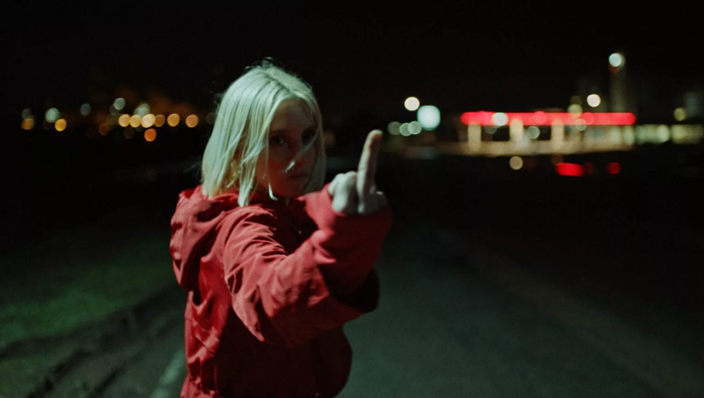Hunted | Vincent Paronnaud Hunted film still: Woman in red jacket flipping the bird at night. Vincent Paronnaud film.