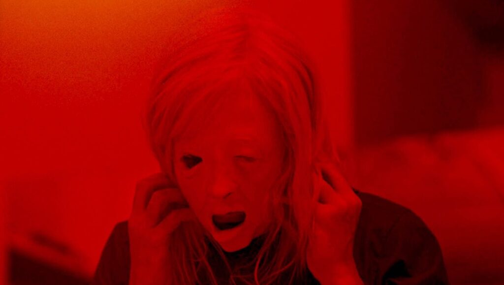 Possessor | Brandon Cronenberg A still from Brandon Cronenberg's *Possessor*. Andrea Riseborough in a red-tinted, distorted close-up. Horror film.