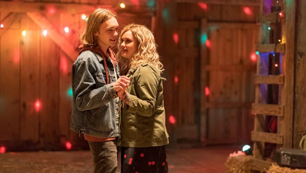 Spontaneous movie scene: Teen couple holding hands, illuminated by string lights in a rustic barn setting.