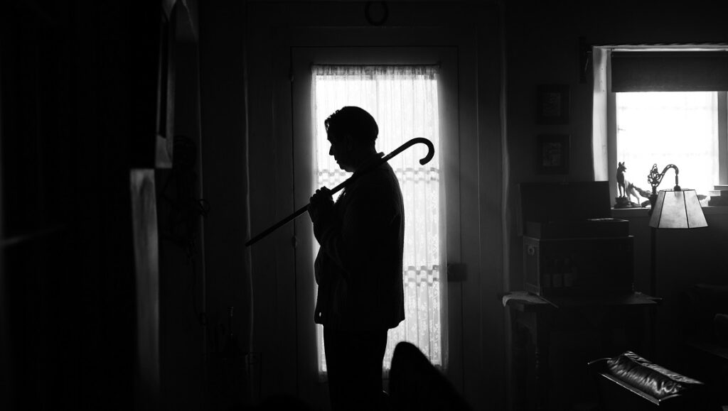 Black and white still from Mank. Silhouette of man with cane in doorway. David Fincher film.