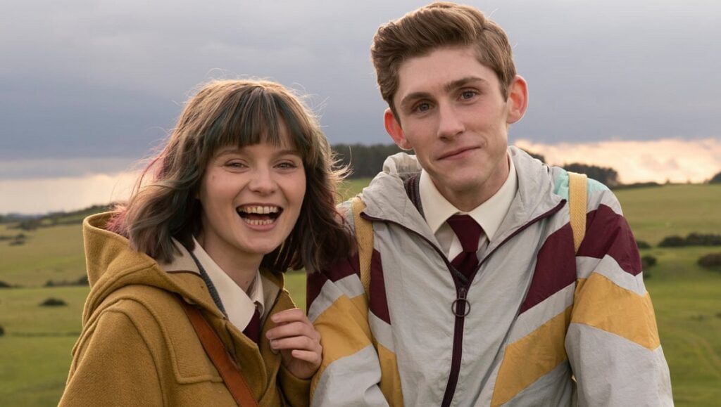 Dating Amber movie still. Two smiling teens, a girl and a boy, stand close together outdoors.