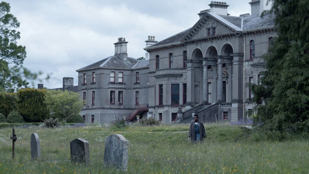 Kindred | Joe Marcantonio Kindred movie scene: A man walks past gravestones toward a large, ominous manor.