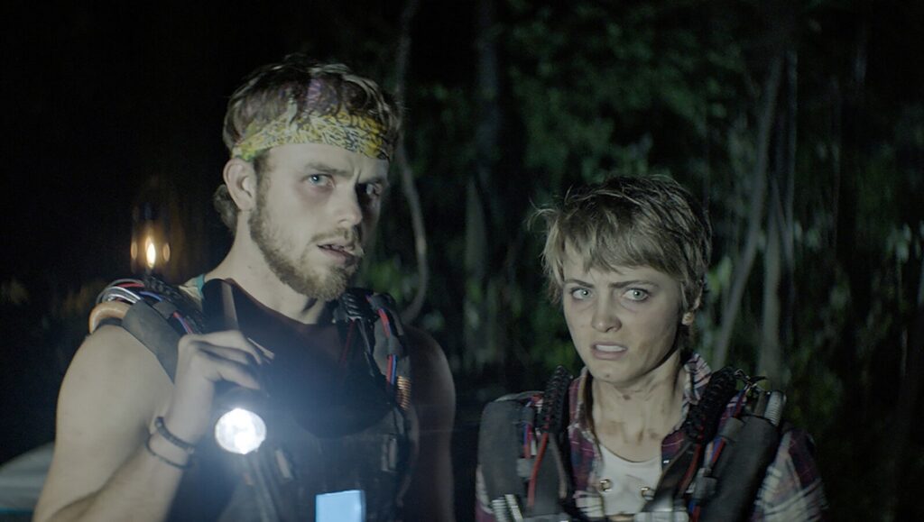 Triggered movie scene: Two scared young adults in the dark, wearing vests, one holding a flashlight.