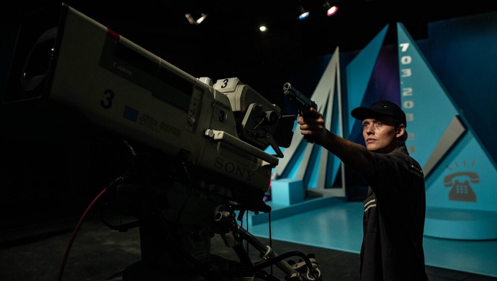 Prime Time | Jakub Piatek Prime Time film still. Man points gun at TV camera in studio. Jakub Piatek film.