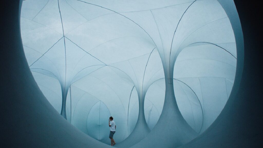 The Reason I Jump film still. Man walks in a white, tunnel-like structure with geometric, arching shapes.