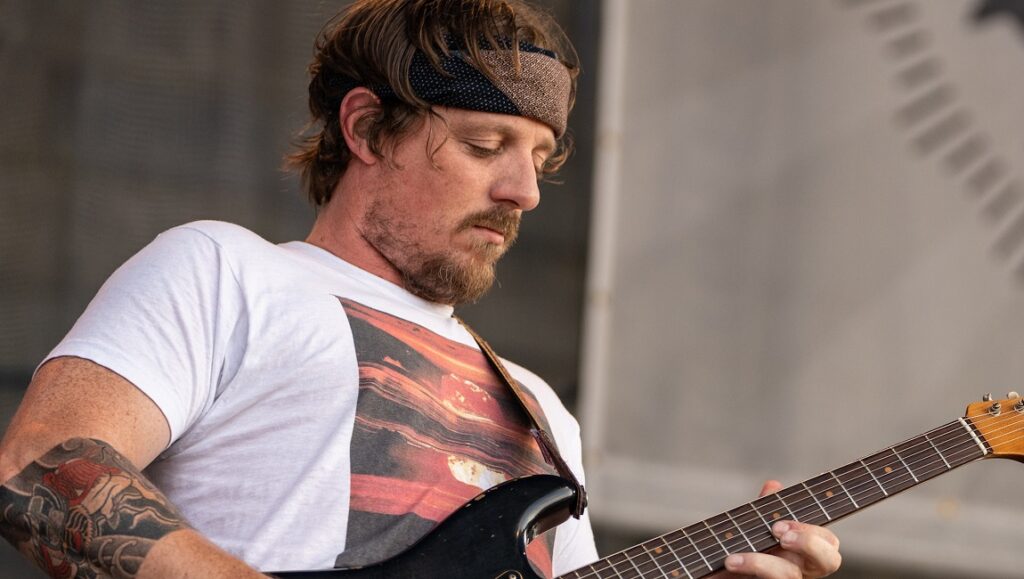 Sturgill Simpson playing guitar. Cuttin' Grass Vol. 1 & Vol. 2 album. Musician with headband and tattoo.