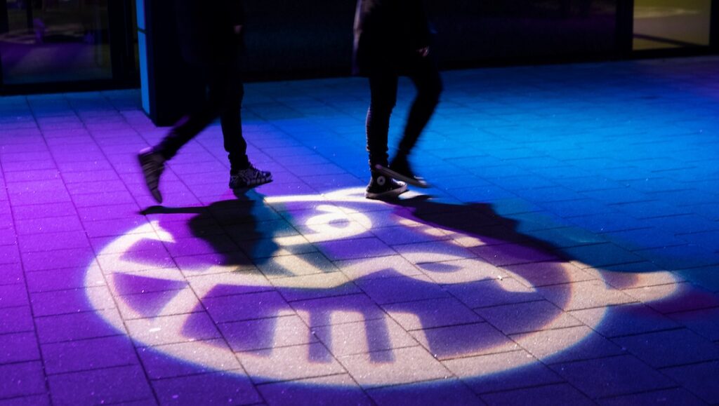 People walking over the IFFR (International Film Festival Rotterdam) tiger logo projected on the ground.