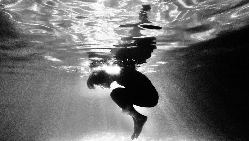 Bipolar film still: Person underwater, curled in fetal position. IFFR 2021 film review. Black and white.