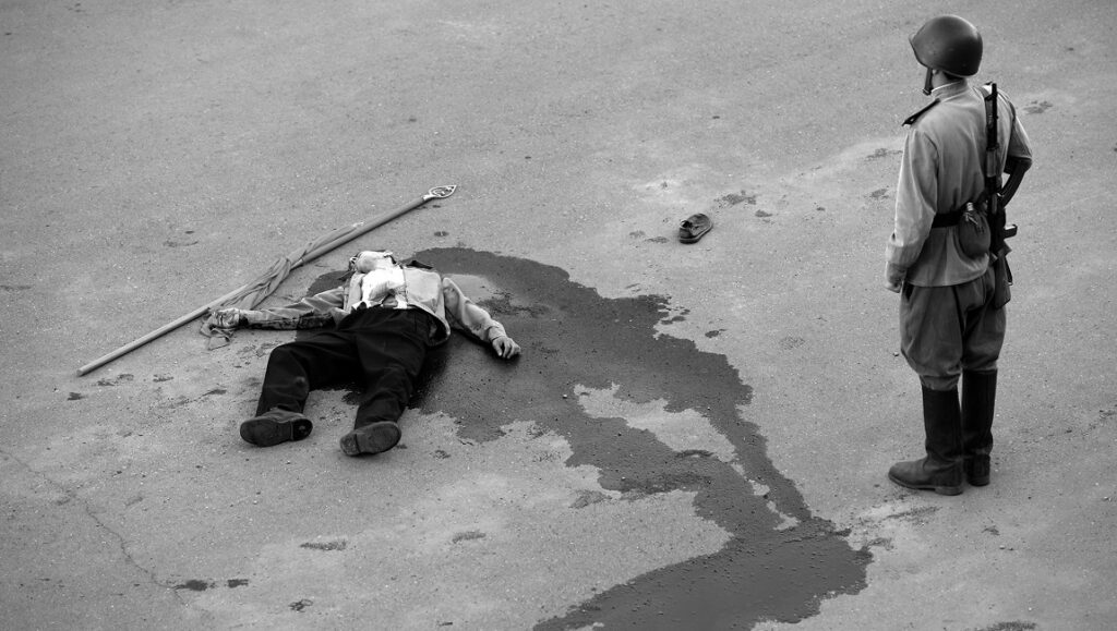 Dear Comrades film still. Soldier stands over a body on the ground. Black and white.