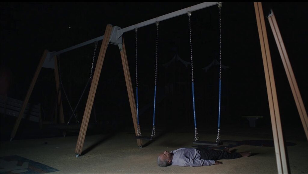 Feast film still: Man lies under swingset at night. IFFR 2021 film review.