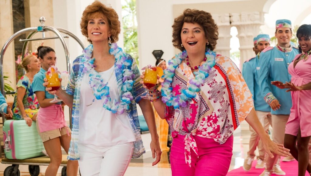 Barb and Star Go to Vista Del Mar | Josh Greenbaum Barb and Star Go to Vista Del Mar movie scene. Kristen Wiig and Annie Mumolo with cocktails and leis.