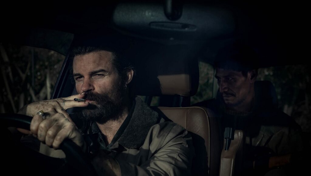 On the Count of Three at Sundance Film Festival: Man smoking in car with passenger. Dark, gritty film still.