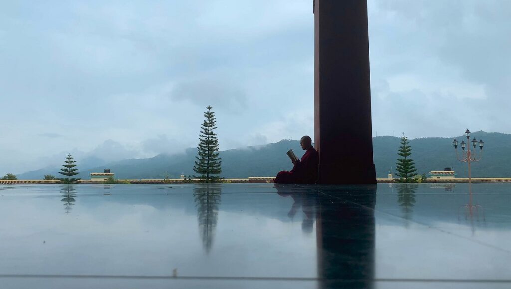 Life in a Day 2020 film still. Monk reading by pillar, mountain backdrop. Sundance Film Festival.