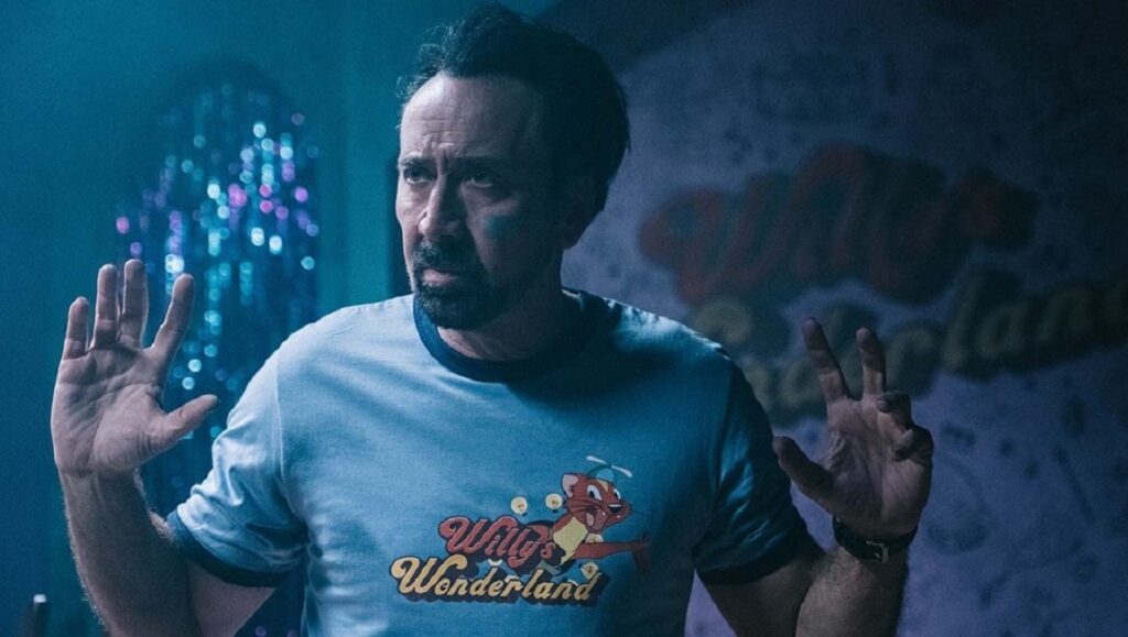 Willy’s Wonderland | Kevin Lewis Nicolas Cage in Willy's Wonderland. Actor with hands raised, wearing Willy's Wonderland T-shirt. Kevin Lewis film.