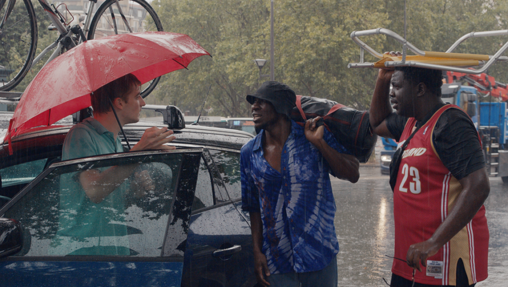 All Hands on Deck | Guillaume Brac Scene from A L'abordage French film, Rendez-Vous with French Cinema 2021. Three men in the rain, one with umbrella.