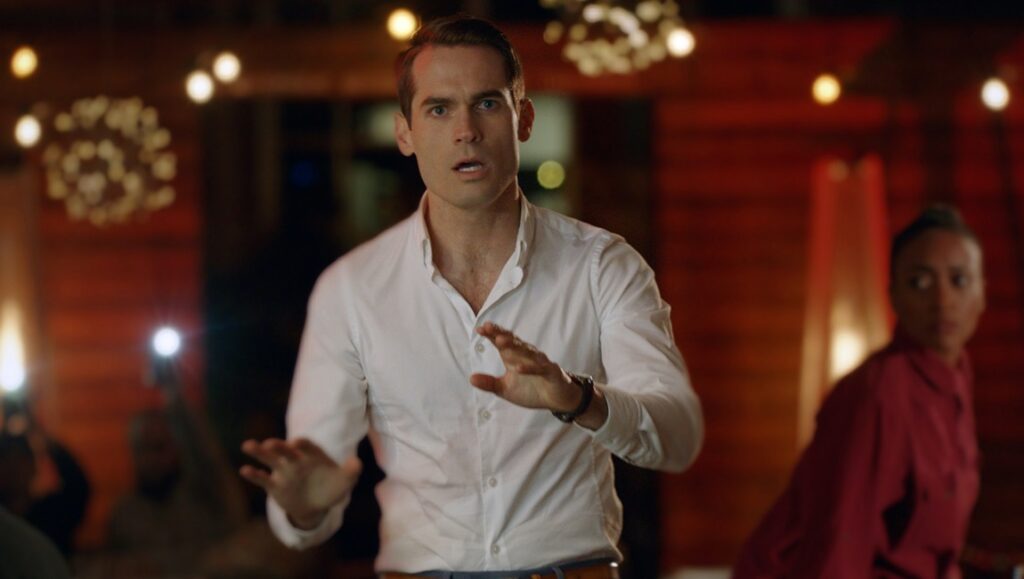 Language Lessons film still from Berlin Film Festival. Mark Duplass gestures with hands. Natalie Morales is in the background.