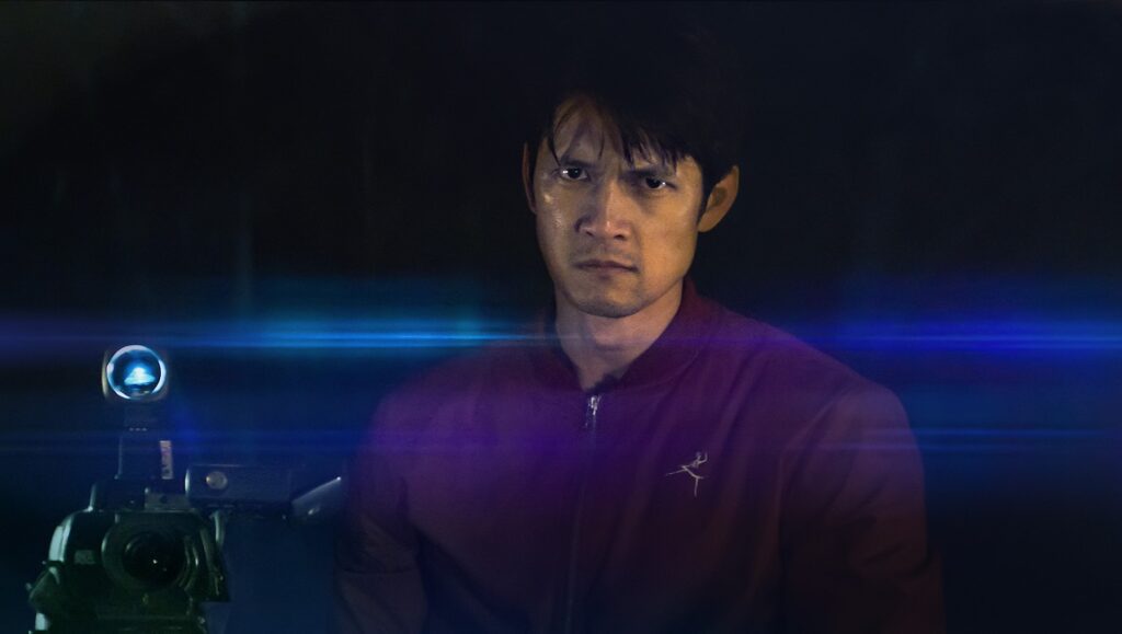 Still from Broadcast Signal Intrusion at SXSW Film Festival. Man in jacket with camera.