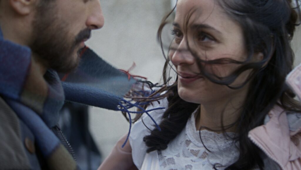 Copilot | Anne Zohra Berrached Copilot film still: A woman smiles at a man in a scarf, close-up. Anne Zohra Berrached film.