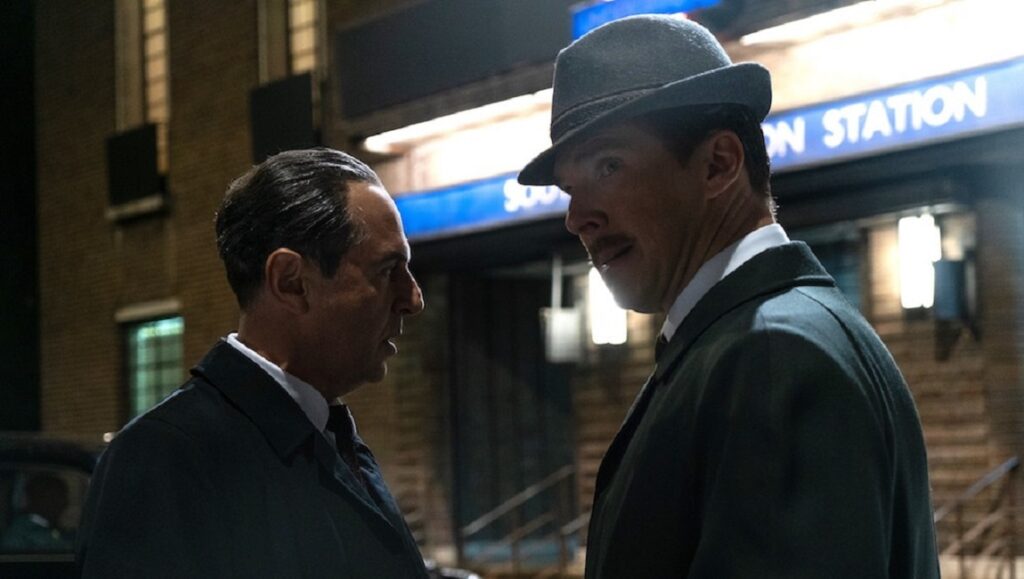 The Courier | Dominic Cooke The Courier movie scene: Benedict Cumberbatch in hat and suit talking to another man at a station.