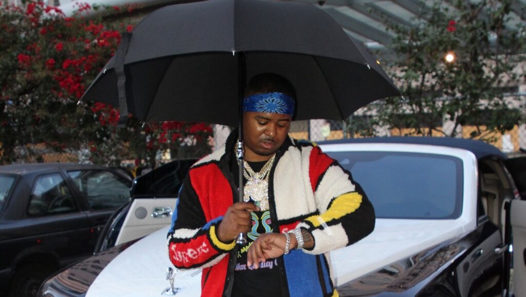 Drakeo the Ruler stands with umbrella, checking watch. Album Roundup February 2021.