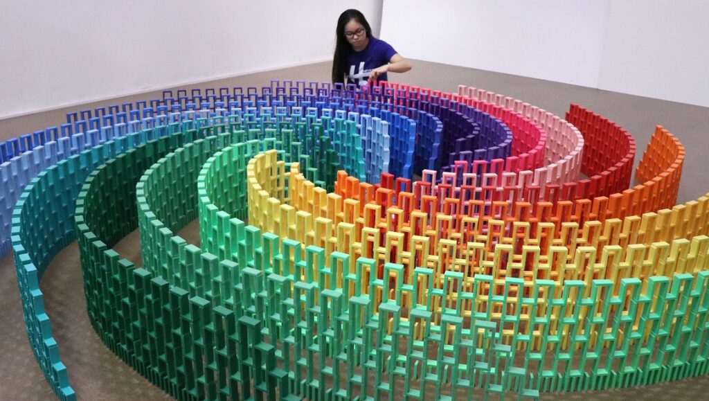 Woman setting up a spiral pattern of colorful dominoes. Domino effect art.