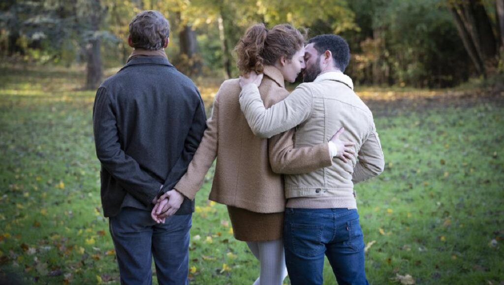 Love Affair(s) film still. Couple embraces in park, unaware of the man behind them. French Cinema 2021.