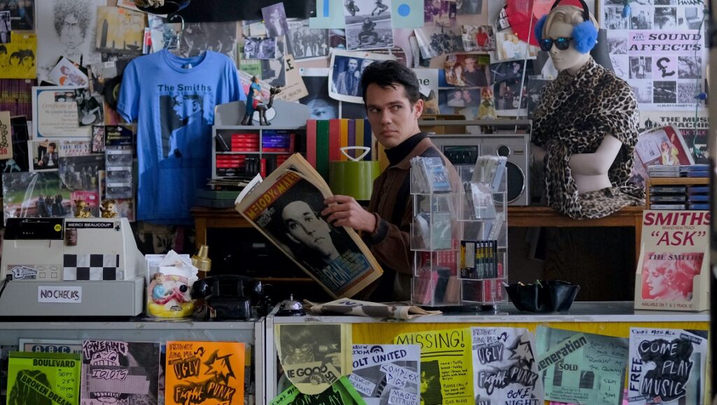 Shoplifters of the World movie scene. Man reading Melody Maker in The Smiths-themed record store. Posters and band merchandise visible.