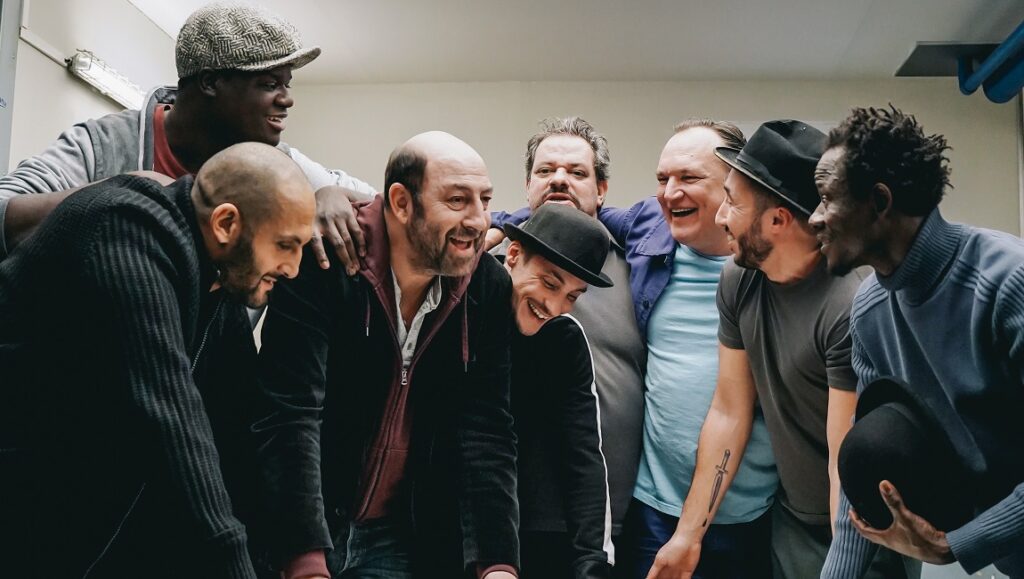 The Big Hit | Emmanuel Courcol Cast of The Big Hit movie. Group of diverse men smiling and looking down. Emmanuel Courcol film.