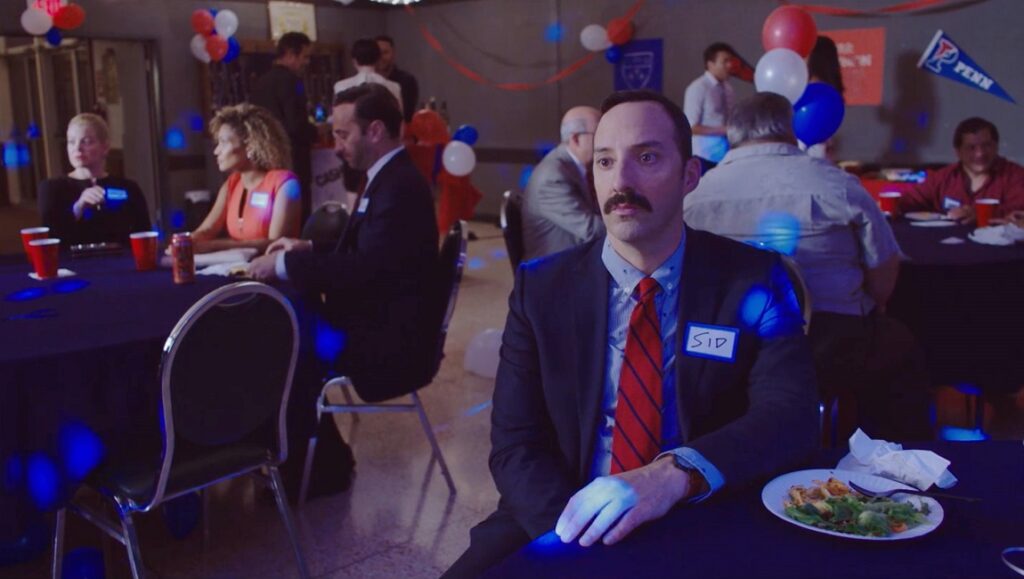 Eat Wheaties! film scene. Man in suit at political event. Patriotic red, white, and blue decorations.