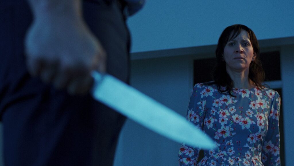 Held | Travis Cluff & Chris Lofing Held movie scene: Woman in floral dress faces a man holding a knife. Thriller, suspense.