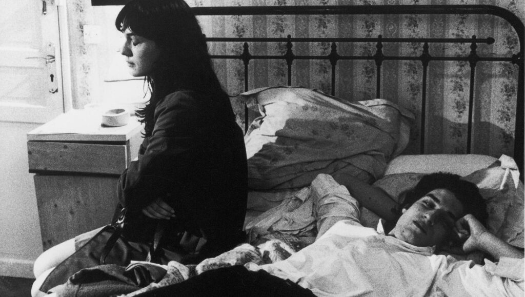 Regular Lovers — Philippe Garrel Regular Lovers film still. Black and white image of a woman sitting on a bed next to a man lying down.