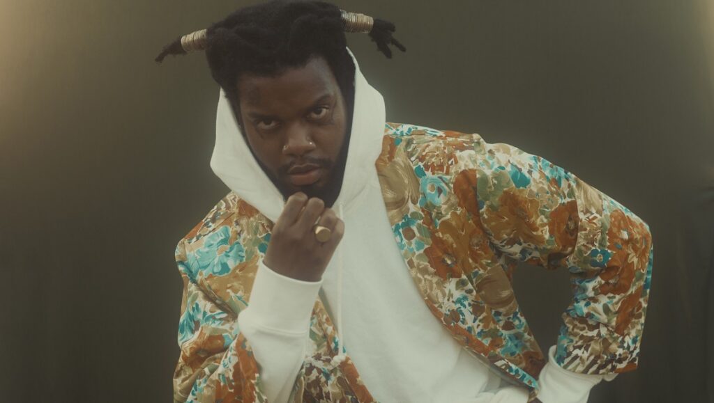 Armand Hammer & The Alchemist - Haram. Serpentwithfeet wearing a floral jacket and white hoodie. Album art.