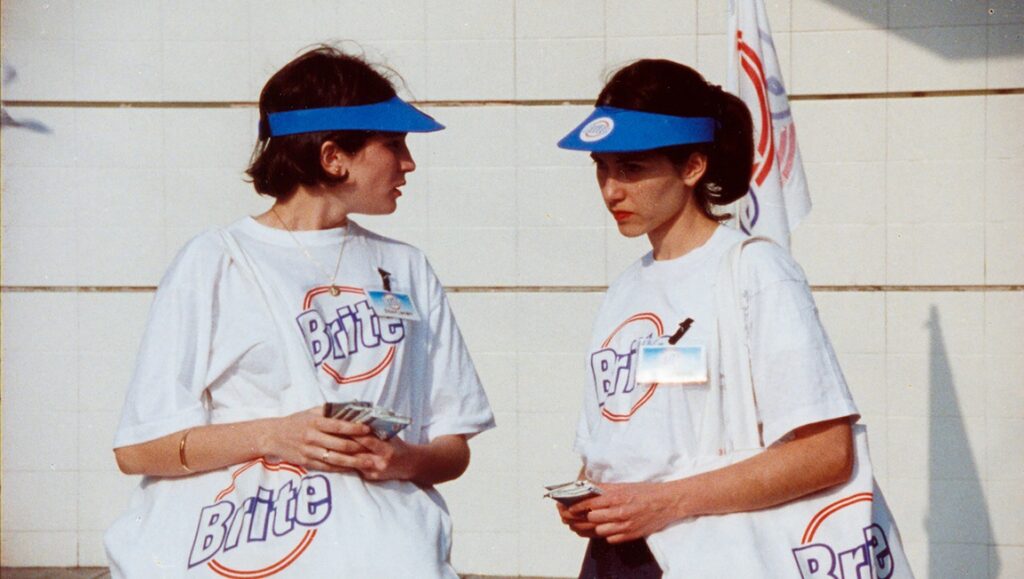 Silvia Prieto still from Neighboring Scenes 2021: Two women wearing Brite t-shirts and blue visors.