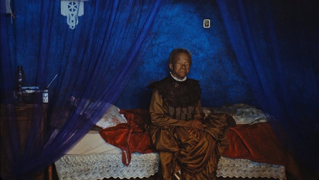 This is Not a Burial, It’s a Resurrection | Lemohang Jeremiah Mosese Still from This Is Not a Burial, It's a Resurrection by Lemohang Jeremiah Mosese. Elderly woman sitting on a bed.