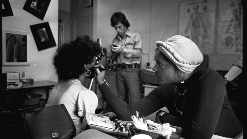 Dope is Death still: Black and white image of a woman receiving acupuncture treatment. Man in background.