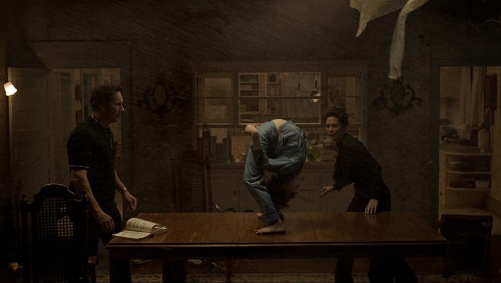 The Conjuring 3: The Devil Made Me Do It scene. Possessed person on table, Ed and Lorraine Warren nearby.