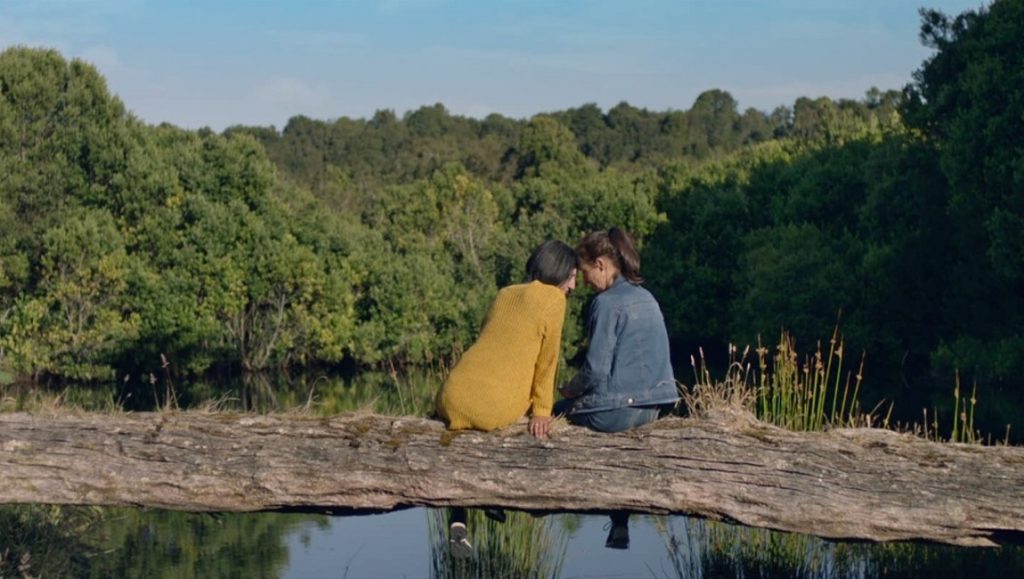 Death Will Come and Shall Have Your Eyes | José Luis Torres Leiva Death Will Come and Shall Have Your Eyes still: Two women sit on a log over water, forest backdrop.