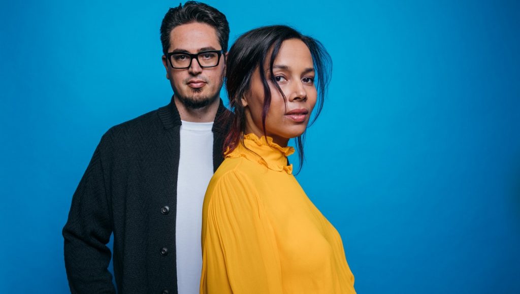 Rhiannon Giddens & Francesco Turrisi | They’re Calling Me Home Rhiannon Giddens album review. Rhiannon Giddens and Francesco Turrisi pose in front of a blue background.