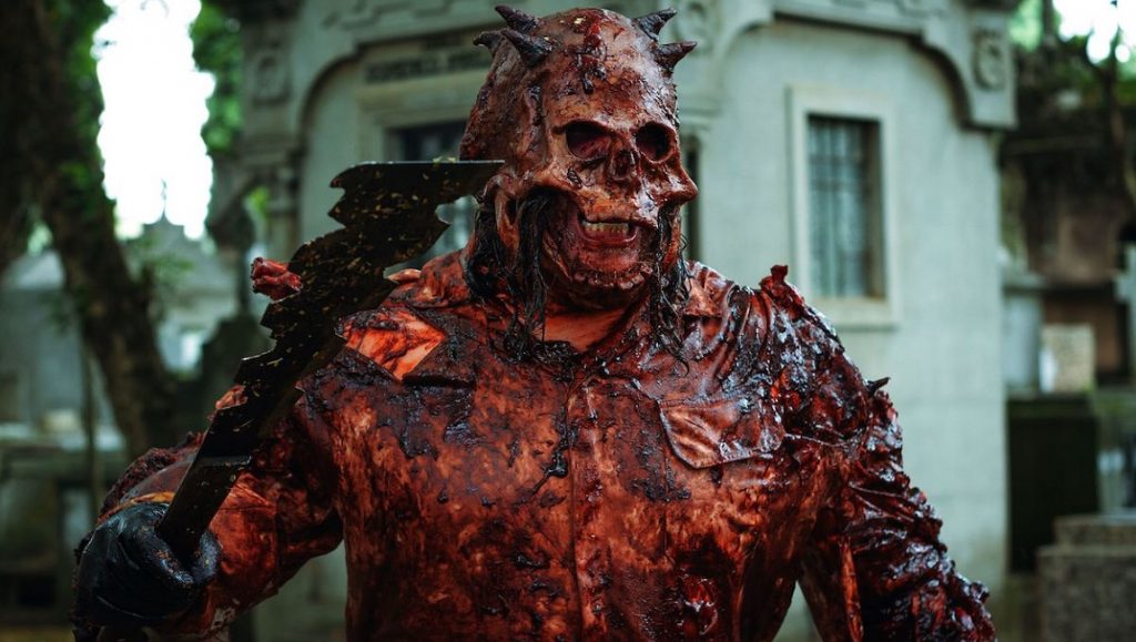 Skull: The Mask | Kapel Furman & Armando Fonseca Skull: The Mask film still. Bloody, horned skull mask wielding an axe. Horror movie character.