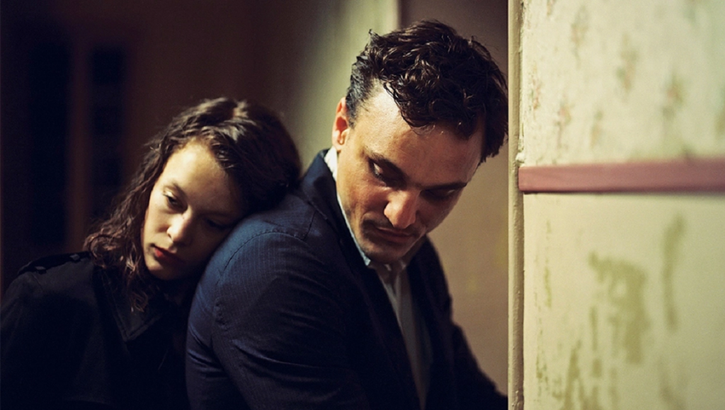 Intimate portrait of a man and woman. Woman leans on man's shoulder. Moody lighting, film photography aesthetic.