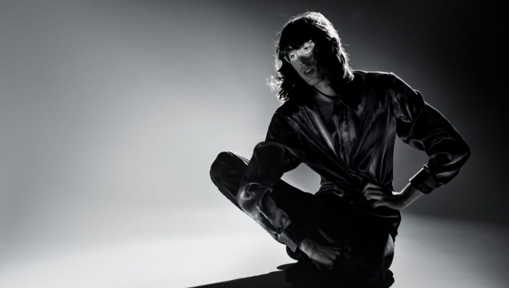 AG Cook | Apple vs. 7G Black and white portrait of A. G. Cook for May 2021 album roundup. Musician in dark clothing crouching.