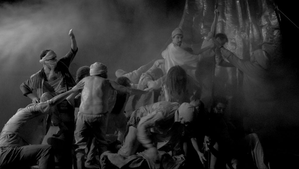 The Belly of the Sea | Agustí Villaronga Black and white film still of El ventre del mar with a group of people in a dark, smoky setting.