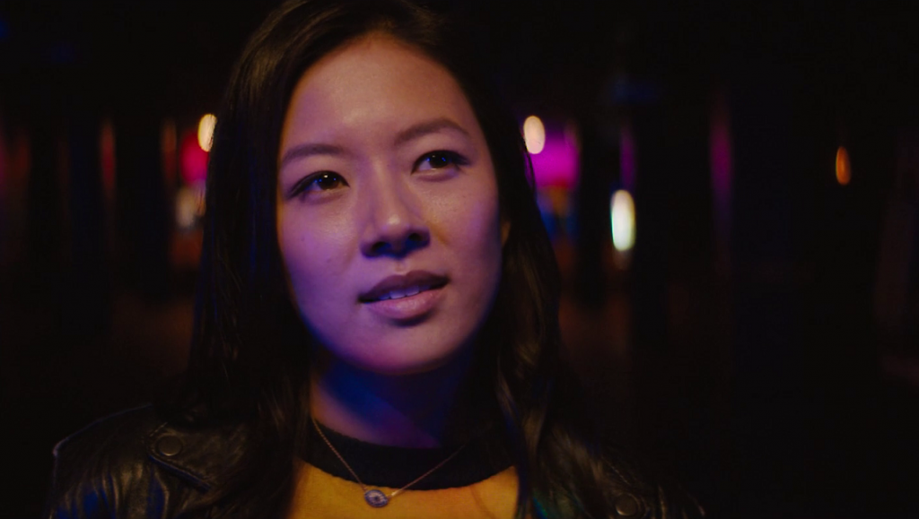 Stalker | Tyler Savage Stalker film still: Woman in leather jacket gazes up, neon lights blur in background.