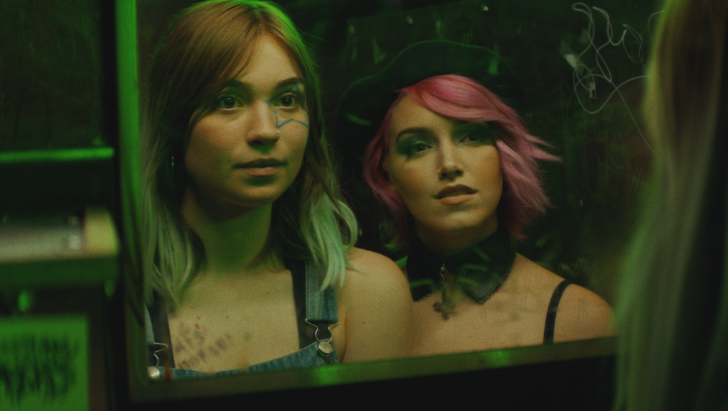 Poser — Ori Segev & Noah Dixon No Man of God film still: Two women reflected in a mirror, one with pink hair and a choker.
