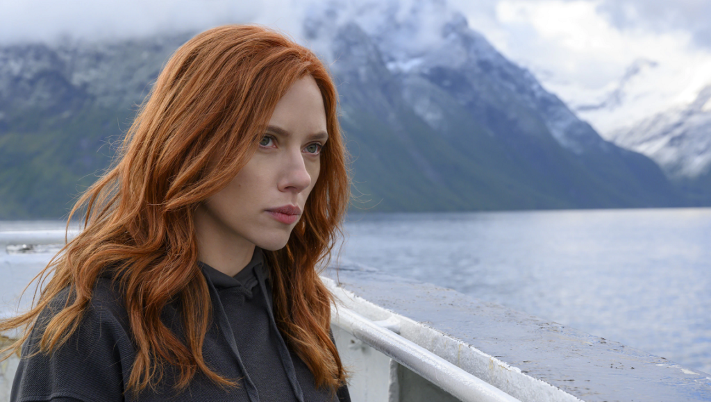 Black Widow | Cate Shortland Black Widow (Scarlett Johansson) gazes pensively. Mountains and water backdrop. Cate Shortland film.